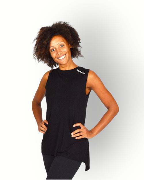 A smiling woman wearing a black sleeveless wide wrap top with a longer back. 