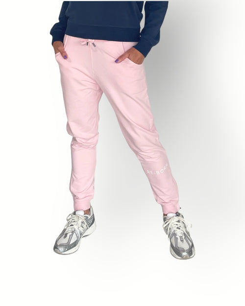 A pair of pink fleece pants with zippers on the legs, featuring side pockets and a ribbed waistband with a drawcord. The pants are modeled by a person wearing a navy top 